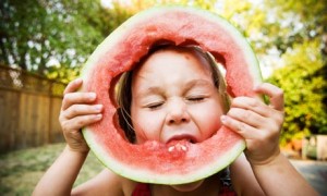 A young girl eating a full slice of watermelon.